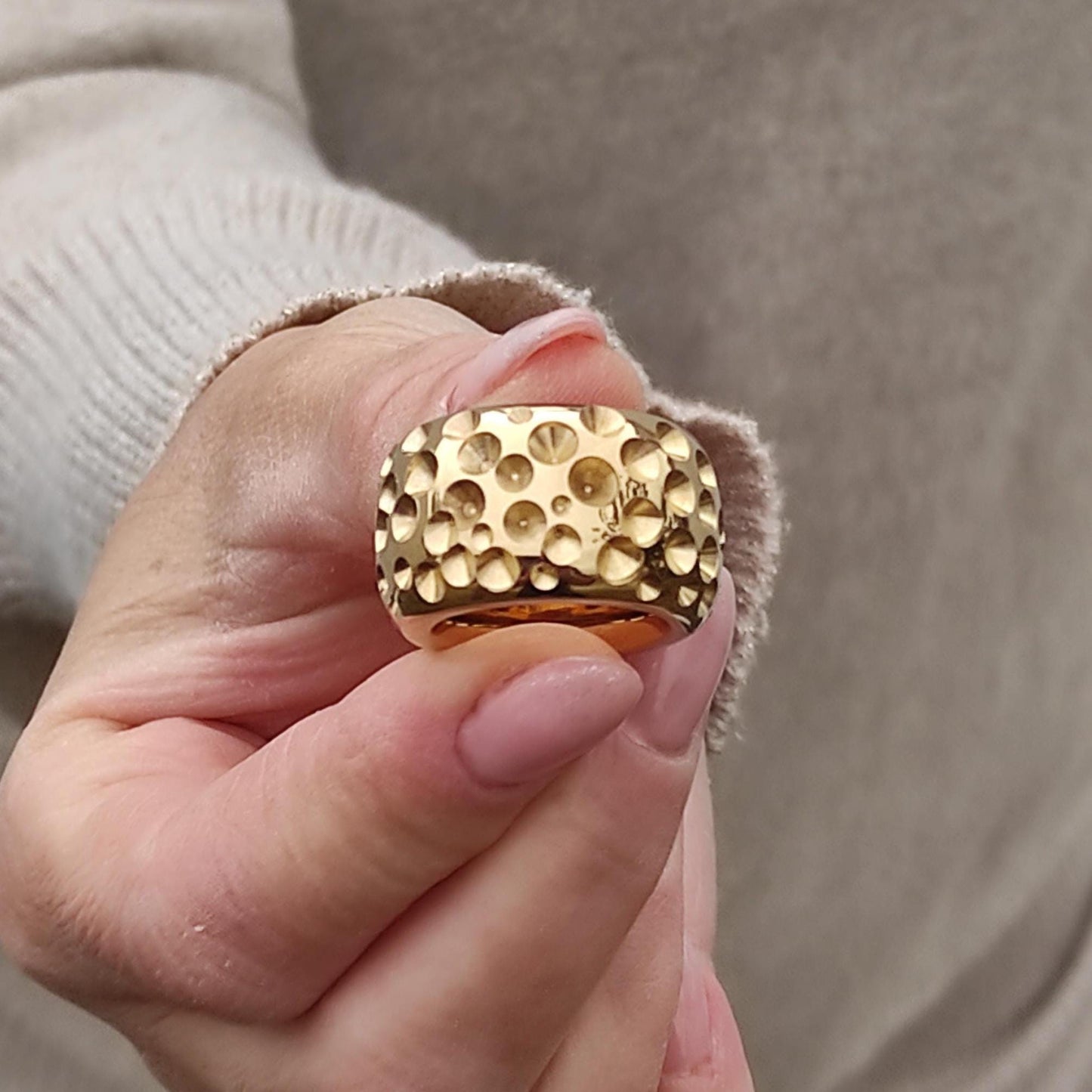 May include: Close-up of a gold ring with a textured surface. The ring has a wide band and a pattern of small, raised circles. The gold ring is a statement piece of jewelry.