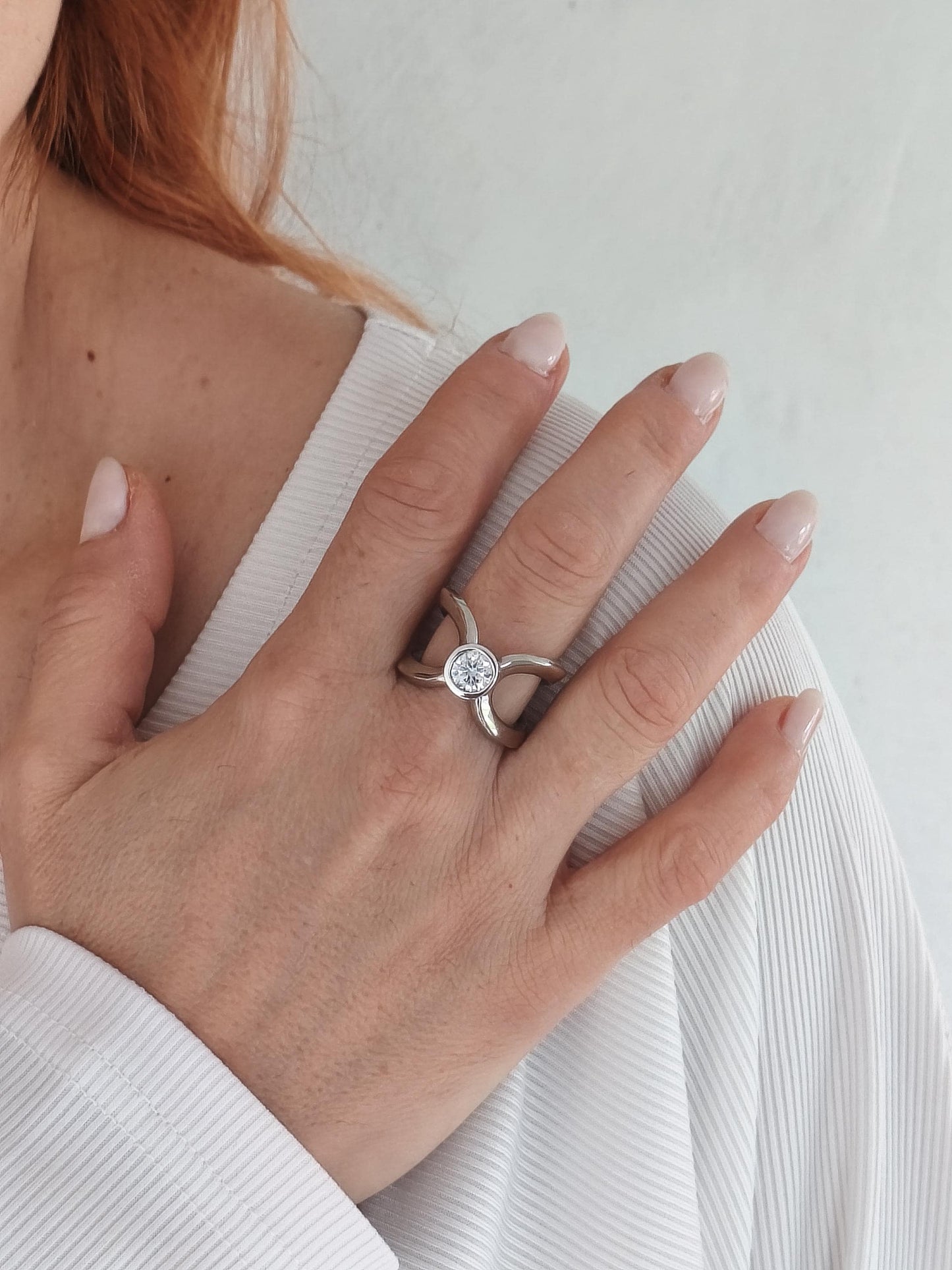 A Palladium coated silver ring with a central, 1Ct moissanite in D color VVS1 clarity. The ring's design features a unique, openwork pattern with curved arms extending from the center. The ring worn is 8US size.