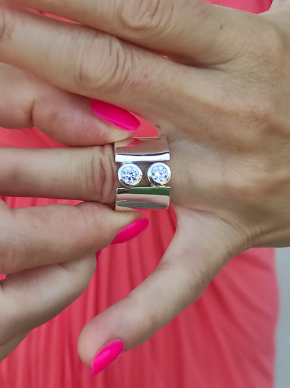 May include: A silver ring with two round clear stones set in a wide band.