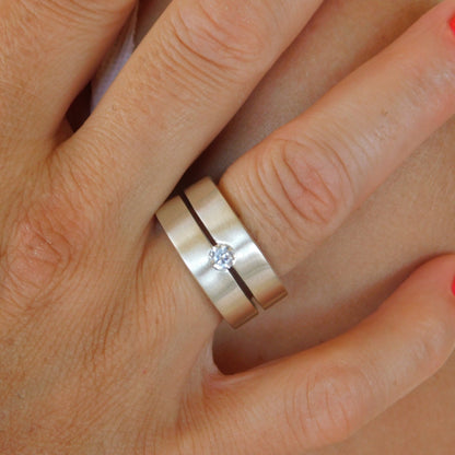 May include: A silver ring with a single, clear gemstone set in the center. The ring is made of two bands that are joined together.