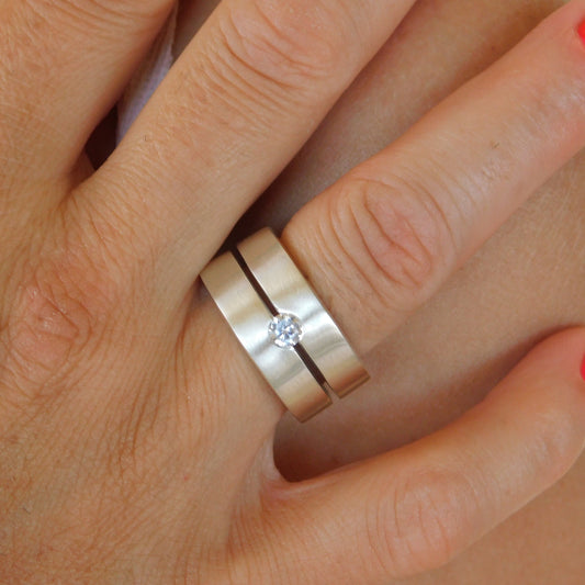May include: A silver ring with a single, clear gemstone set in the center. The ring is made of two bands that are joined together.