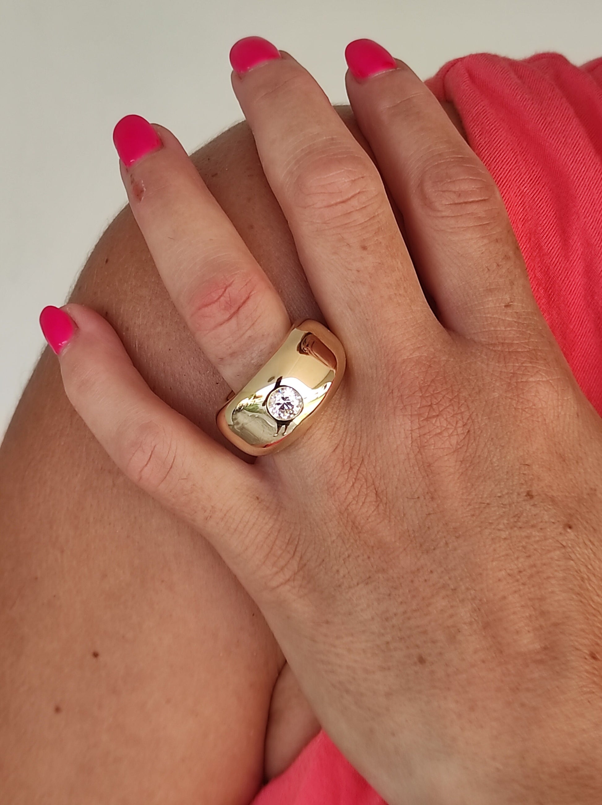 May include: A gold ring with a large, clear, round gemstone set in the center. The ring is thick and has a rounded, dome-like shape.