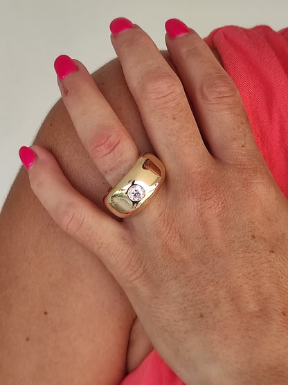 May include: A gold ring with a large, clear, round gemstone set in the center. The ring is thick and has a rounded, dome-like shape.