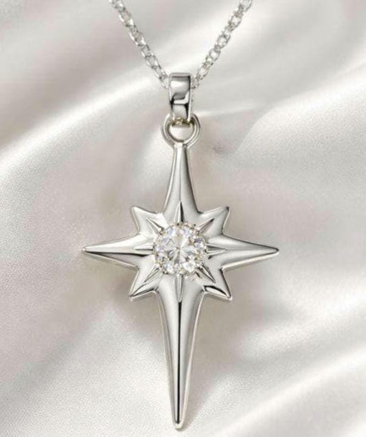 May include: A silver-toned necklace with a starburst pendant. The pendant features a central, round, clear gemstone and a multi-pointed star design. The necklace hangs on a delicate chain, set against a white, silky background.