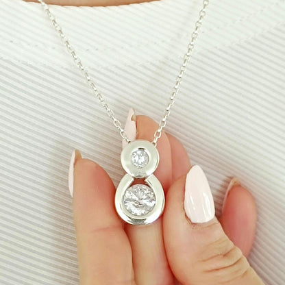 May include: A silver necklace with a pendant featuring two clear, round gemstones. The pendant is suspended from a delicate chain. The gemstones are set in a silver bezel setting. The necklace is displayed against a white background.