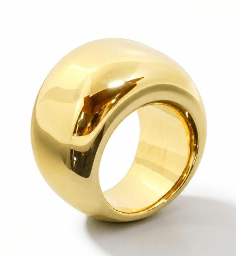 May include: A polished gold-tone ring with a wide, thick, and rounded dome-shaped band. The surface of the ring is smooth and reflective, showing clear highlights and shadows that emphasize its curved, chunky, and solid circular form.