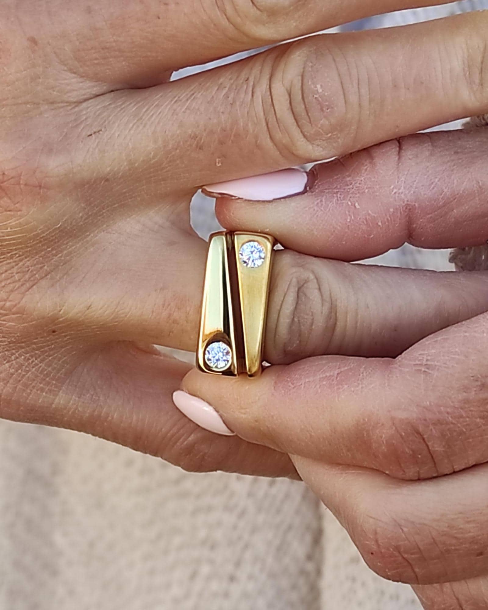 May include: A gold ring with two small diamonds set in the band. The ring is worn on a finger.