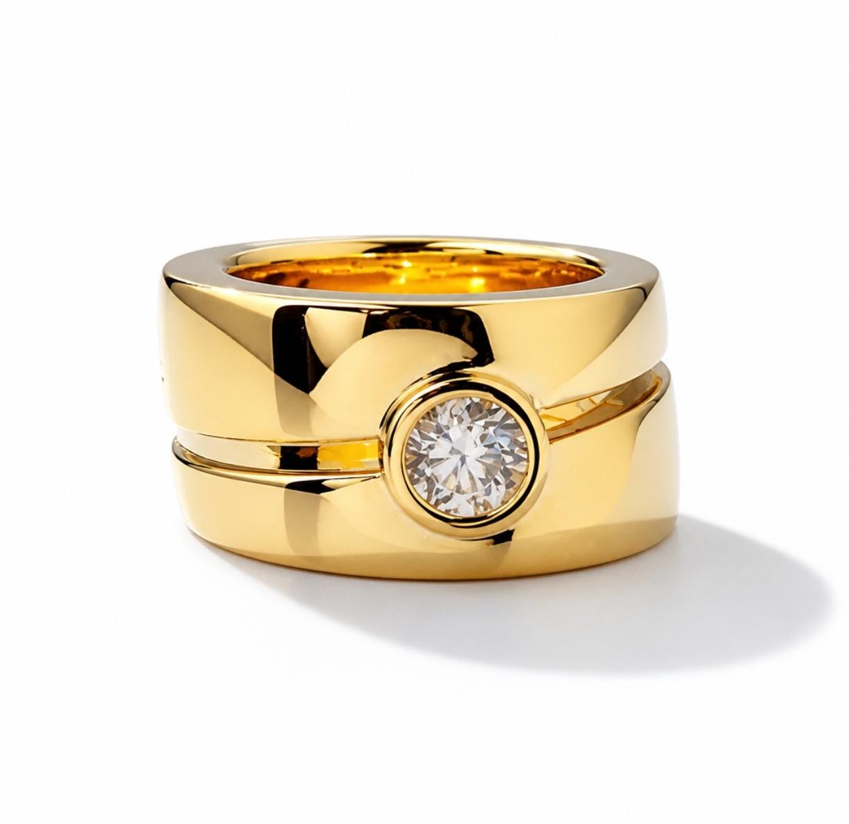 May include: A wide, polished yellow gold band ring featuring a split design with a single, round, brilliant-cut clear gemstone set in a bezel setting at the center. The ring has a smooth, reflective surface and a thick, substantial profile.
